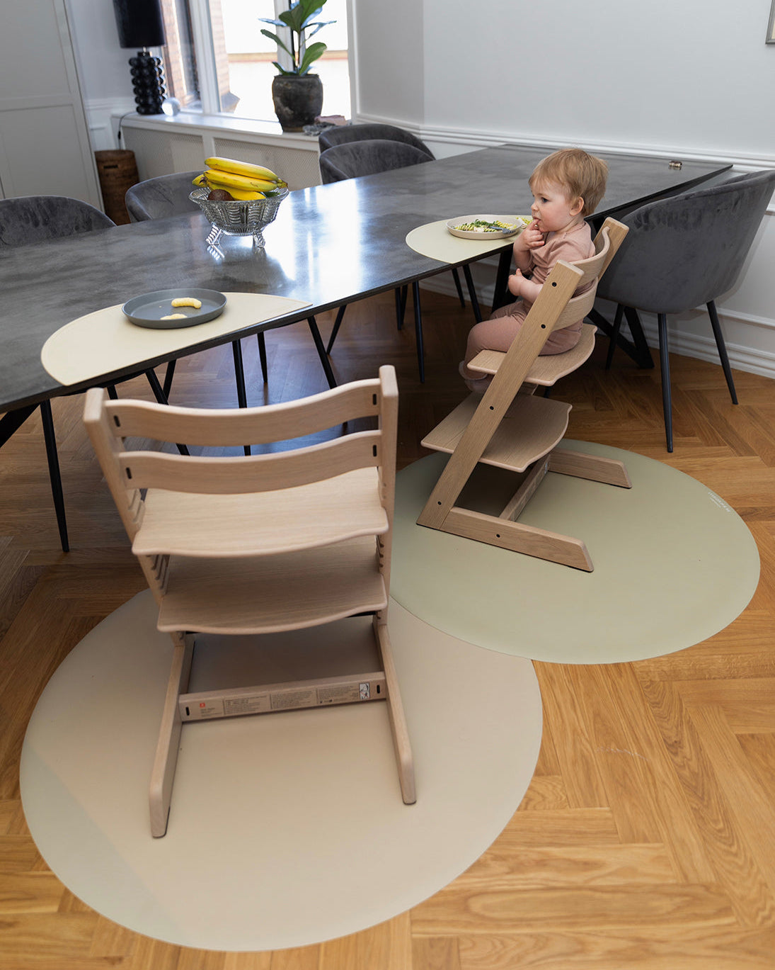 To små børn sidder og spiser på Stokke højstole, mens slidstærke stoleunderlag fra Everleigh and Me i farven Clay beskytter gulvet mod madrester. Underlagene tilføjer både praktisk beskyttelse og et stilfuldt touch til det designinspirerede hjem, stoleunderlag baby, måtte under højstol, underlag til højstol, everleigh and me underlag